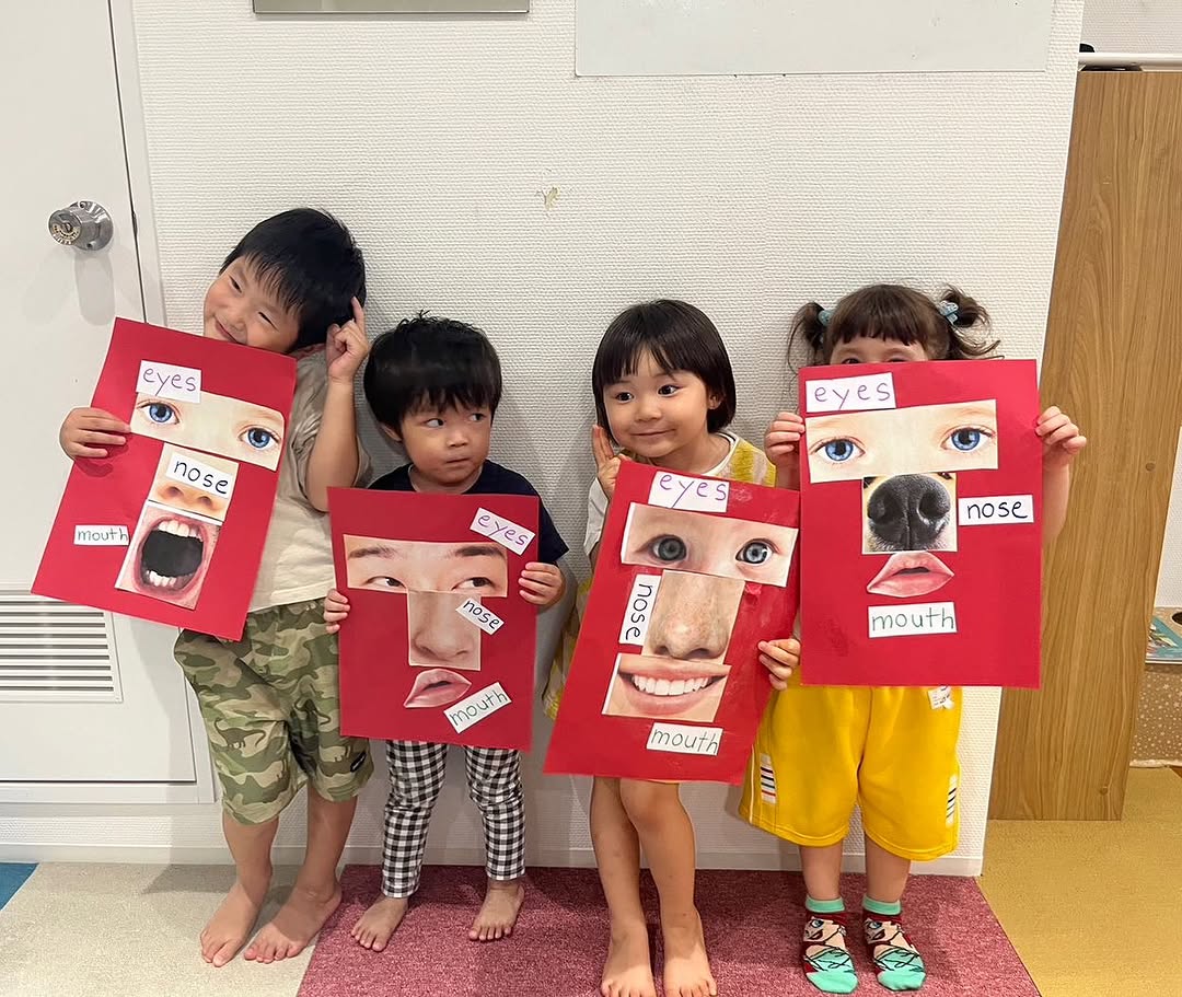 英語で顔のパーツ（eyes・nose・mouth）を学ぶ工作を見せる子どもたち